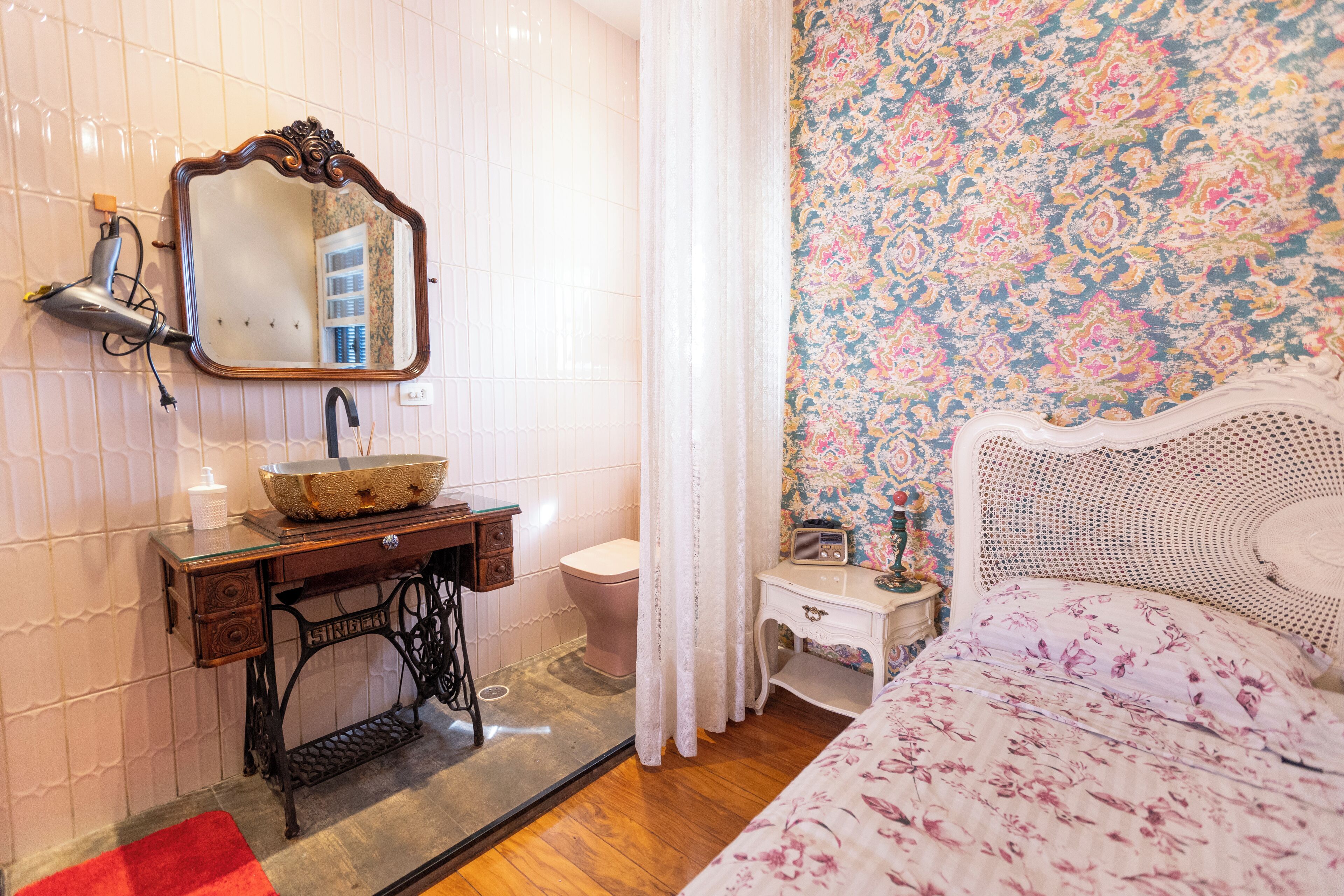 A bathroom with a vintage sewing machine, a sink with a mirror, a toilet, and a radio on a bedside table.