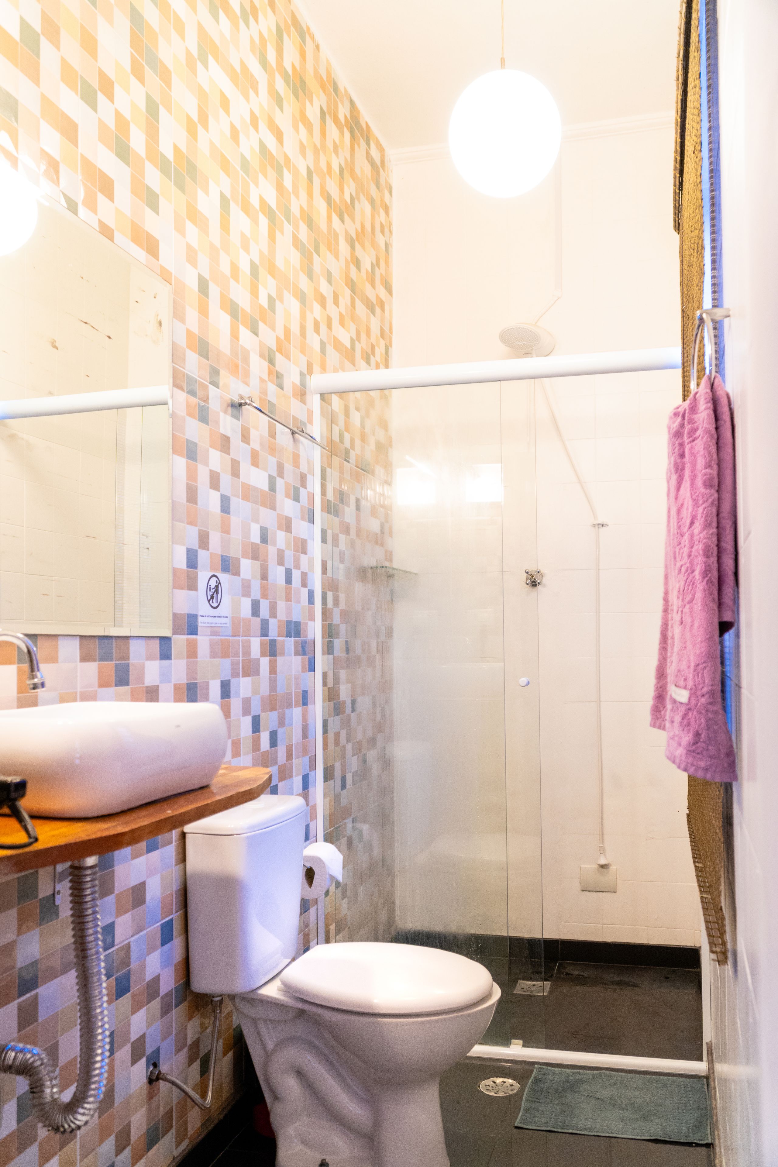 Une salle de bain avec un mur carrelé, des toilettes, un lavabo, une douche et une serviette suspendue.
