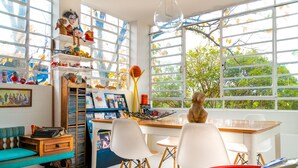 Una habitación con un ventanal grande, un escritorio, sillas y estanterías con diversos objetos.
