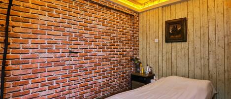 A room with a brick wall, a wooden panel wall, a bed, a nightstand, and a framed picture.
