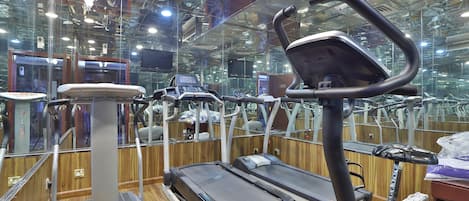A gym with various exercise equipment, including treadmills and elliptical machines, with a wooden floor and mirrored walls.