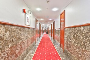 Un couloir d’hôtel avec un tapis rouge, des murs en marbre et des portes en bois.