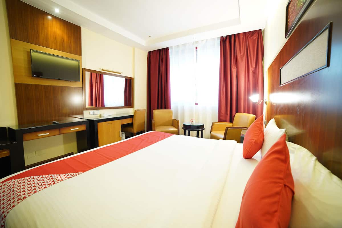 A hotel room with a large bed, a desk, a chair, a television, and a window with curtains.