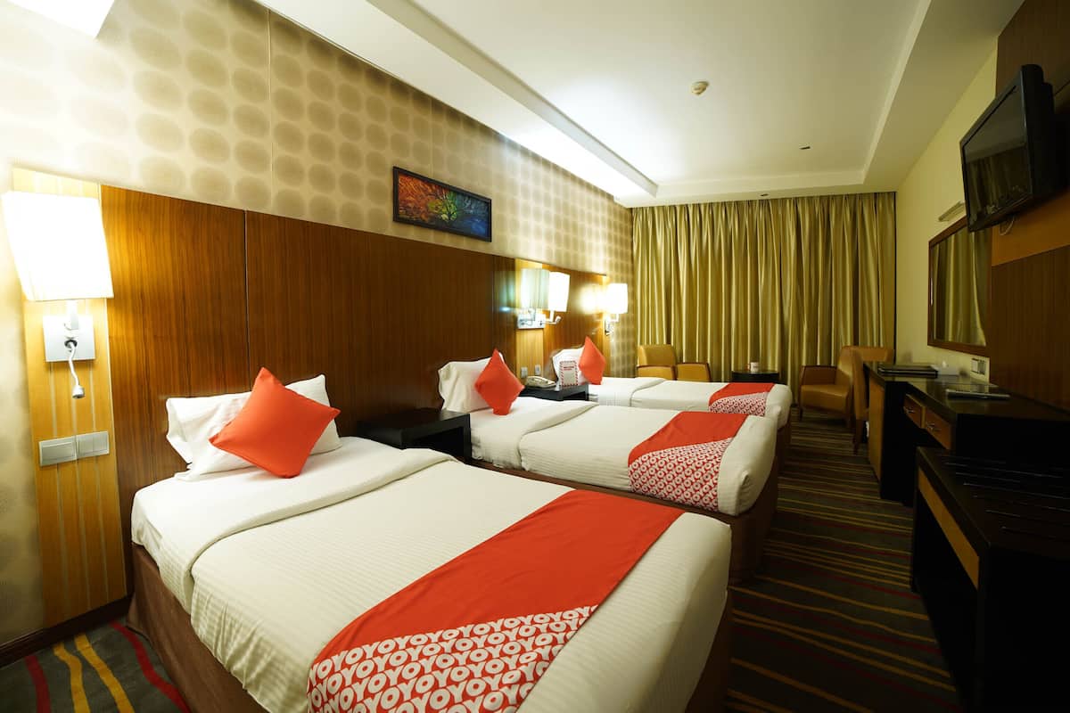 A hotel room with three beds, a desk, a TV, and a bathroom.