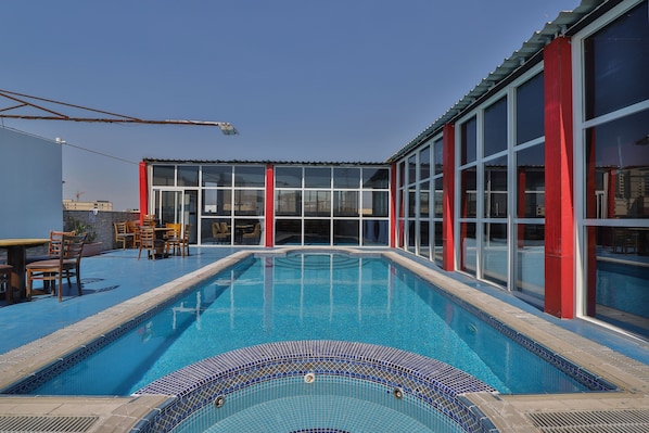 Une piscine dont le bord est recouvert de carreaux, entourée de murs rouges et blancs, et un espace détente avec des chaises.