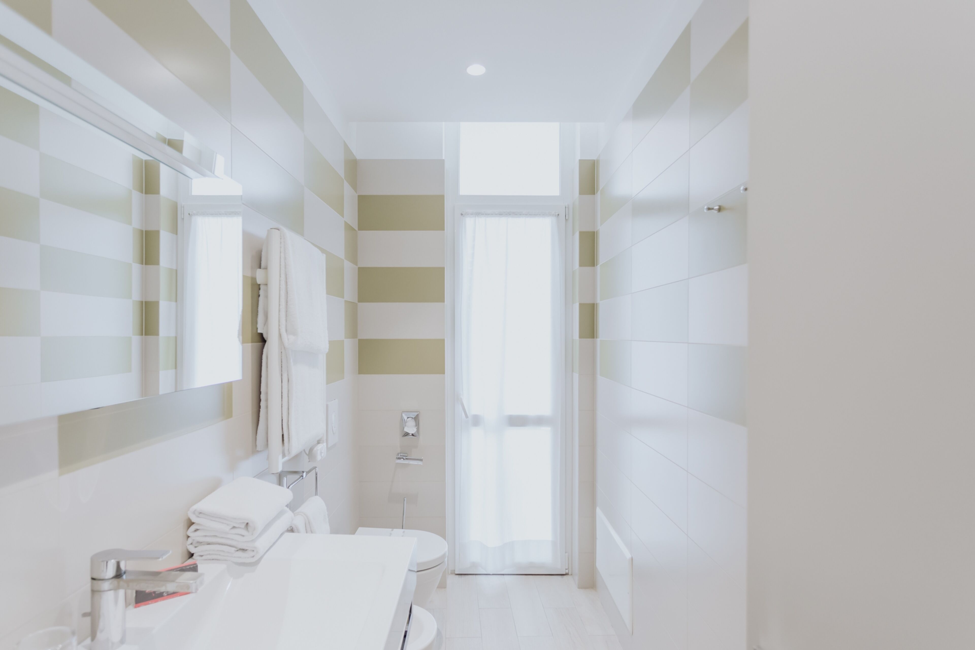 A modern bathroom with a striped tile wall, a white sink, and a toilet.