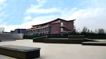 A skatepark with concrete benches and ramps, a modern building with balconies, and a clear sky.