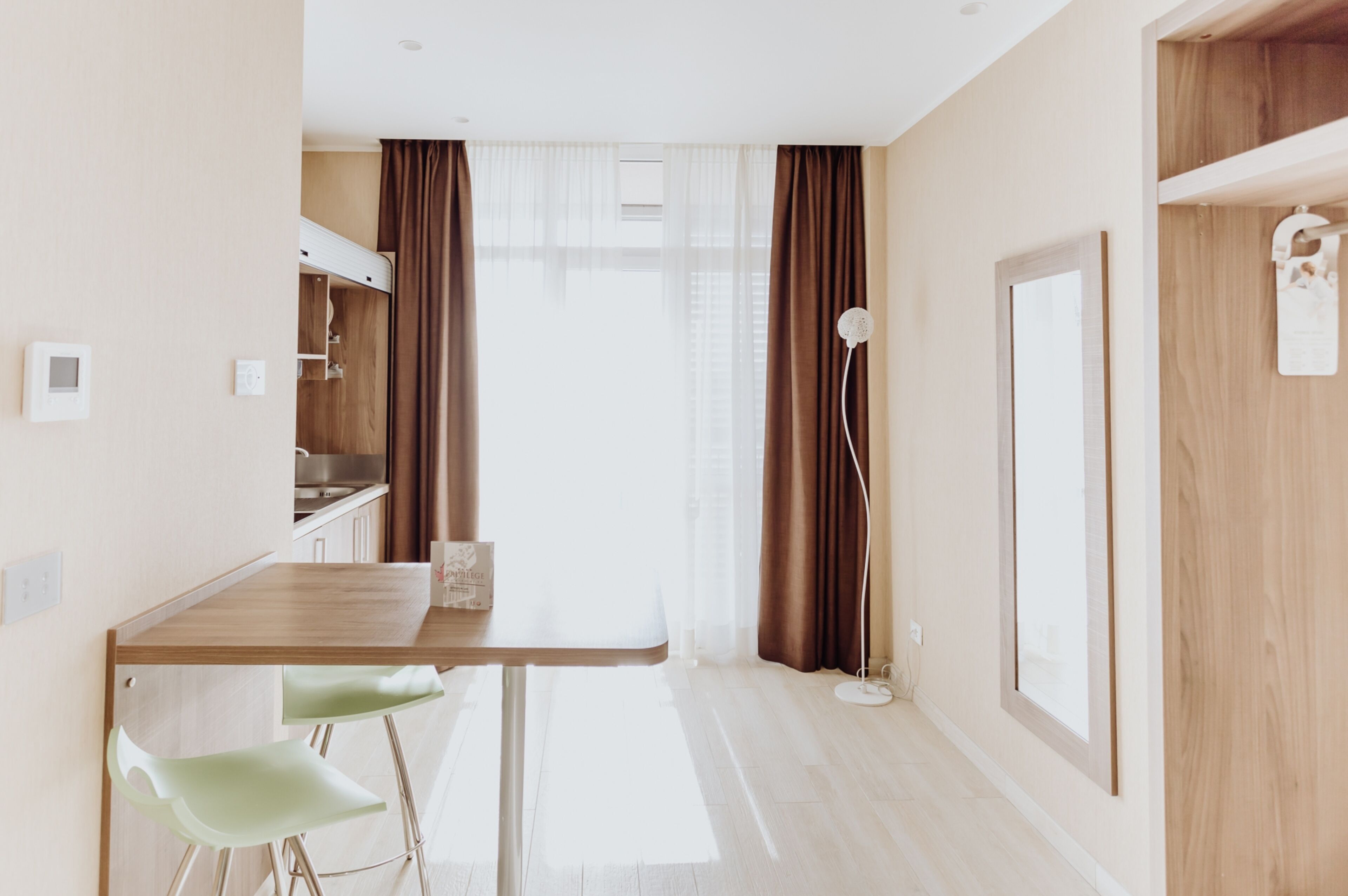 A modern kitchen with a wooden table, two green chairs, and a view of the adjacent living area.