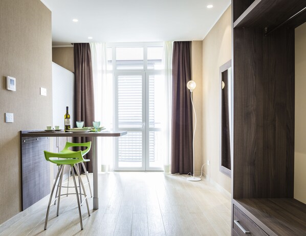 A modern kitchen with a dining area, featuring a bar stool, a table with a bottle, and a view through a glass door. - Privilege Apartments (Vimercate)