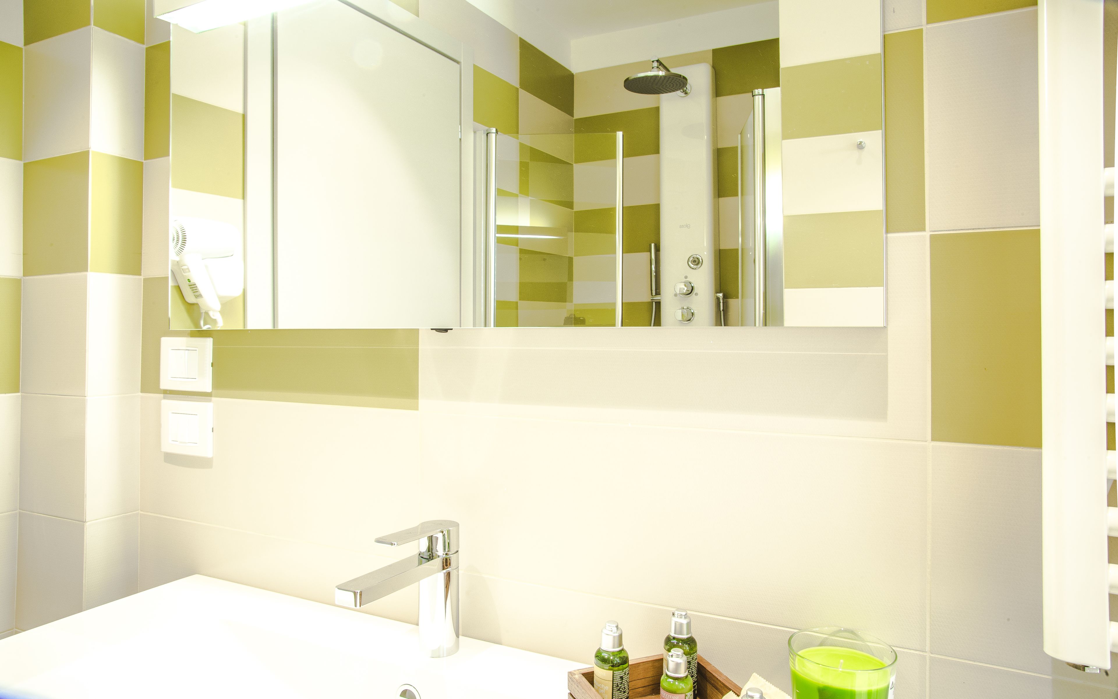 Une salle de bain avec un lavabo blanc, un miroir et une douche. On y trouve des articles de toilette sur le comptoir.