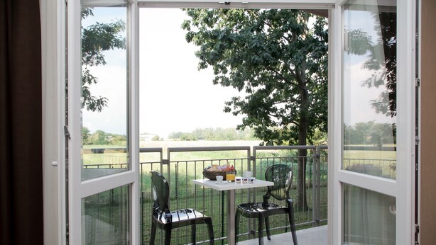 A balcony with two chairs and a table, a glass door, and a view of a green landscape. - Privilege Apartments (Vimercate)