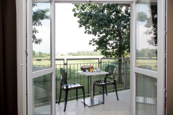 A balcony with two chairs and a table, a glass door, and a view of a green landscape. - Privilege Apartments (Vimercate)