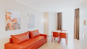 A modern living room with a red sofa, a dining table with chairs, and two framed pictures on the wall. - Privilege Apartments (Vimercate)
