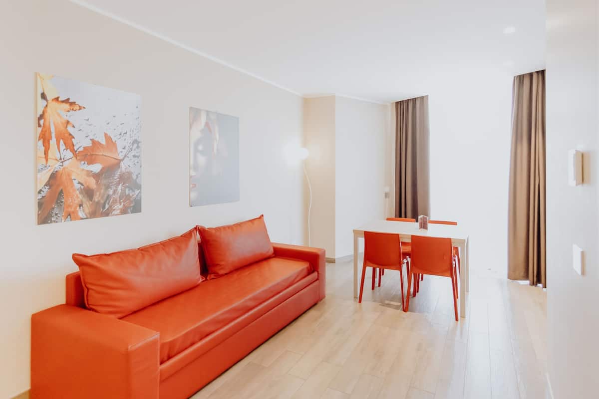 Una sala de estar moderna con un sofá rojo, una mesa de comedor con sillas y dos cuadros en la pared.