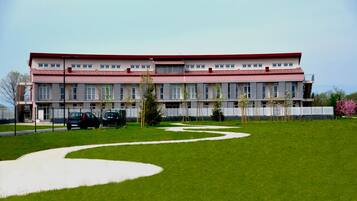 Un edificio grande con tetto rosso e numerose finestre. C'è un prato verde con un vialetto sinuoso e alcuni alberi.