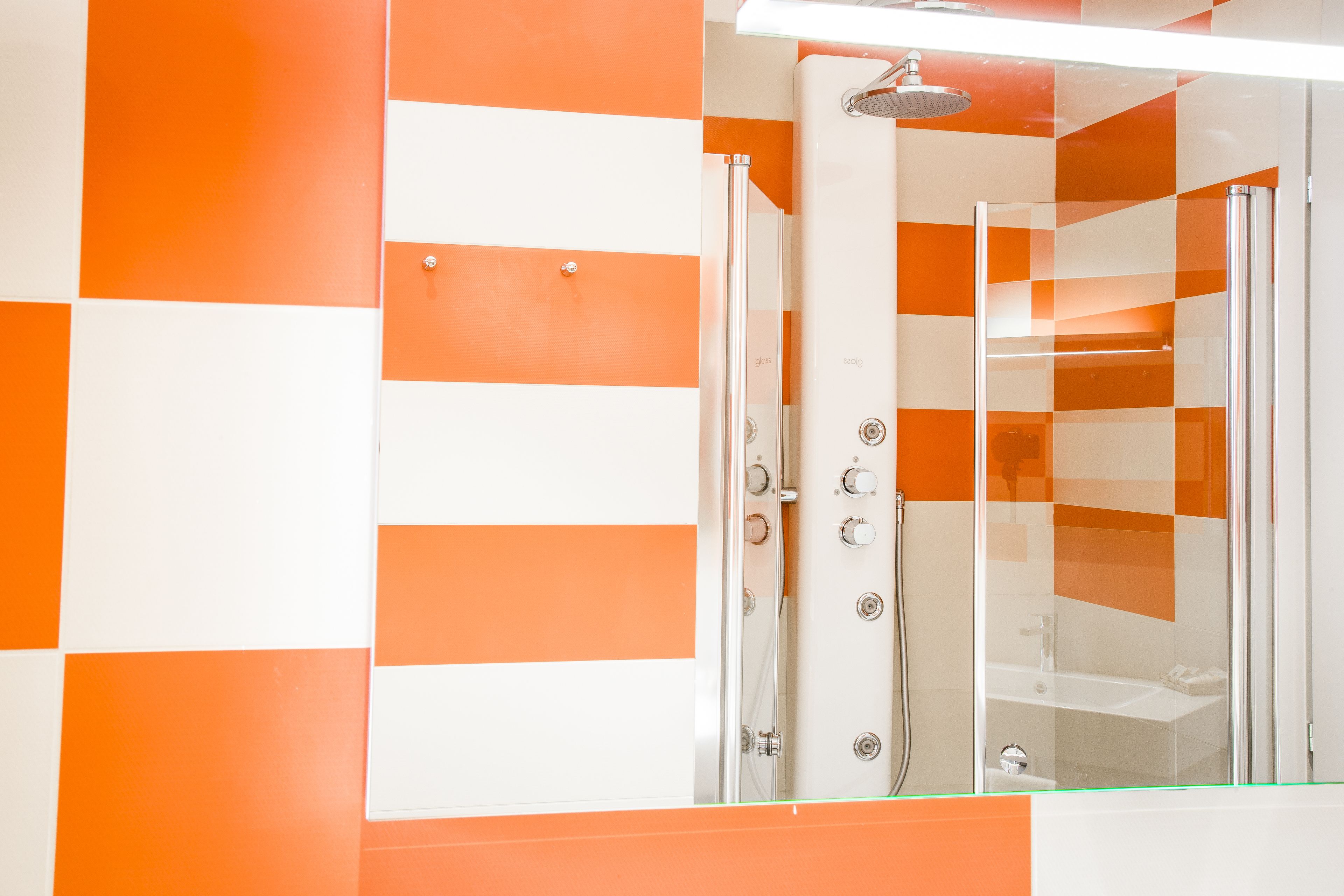 A bathroom with orange and white checkered walls, a glass shower enclosure, and a visible sink.