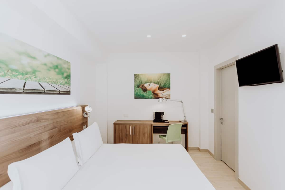 Habitación de hotel con cama, escritorio, silla, televisor y obras de arte en las paredes.