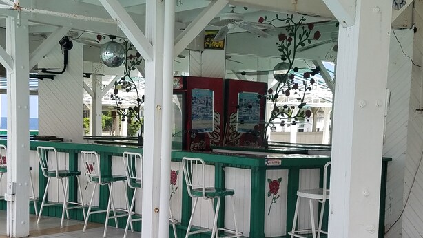 Un espacio al aire libre con asientos techados, sillas blancas y verdes, una máquina expendedora de Coca-Cola y una bola de discoteca.