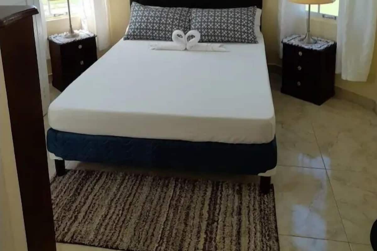 Un dormitorio con cama, dos lámparas de noche, una ventana con cortinas y una puerta.