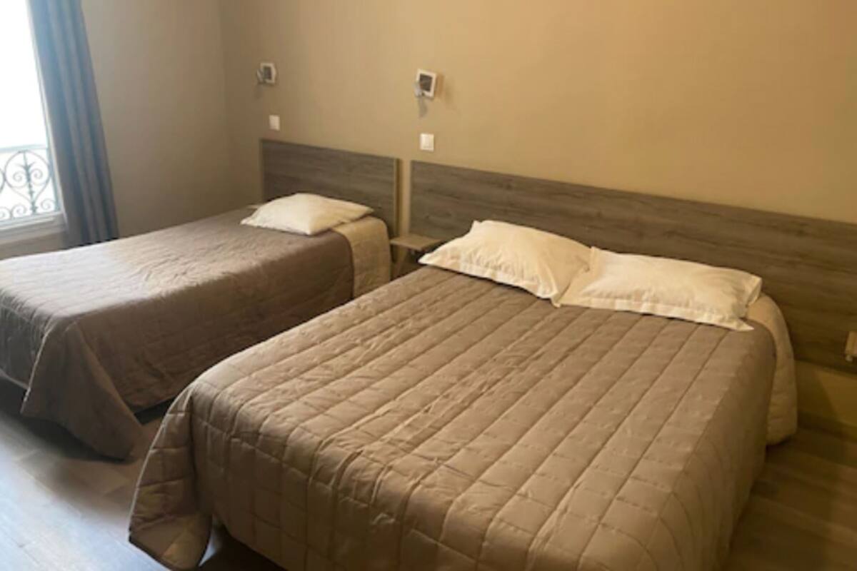 Two single beds with headboards, a window with curtains, and a wall-mounted light fixture.