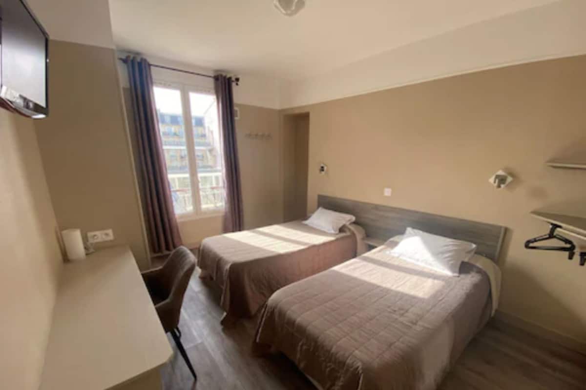 A hotel room with two beds, a desk, and a window with curtains.