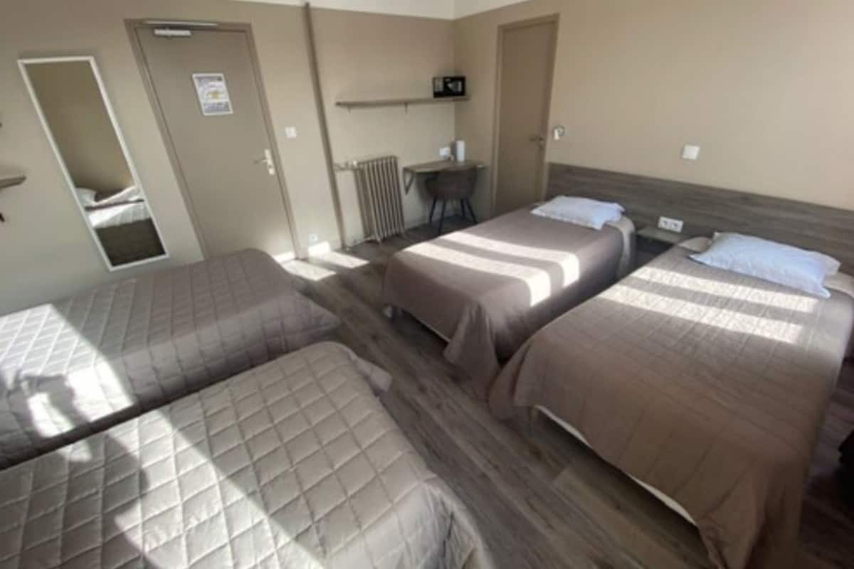 A hotel room with three beds, a desk, and a radiator.