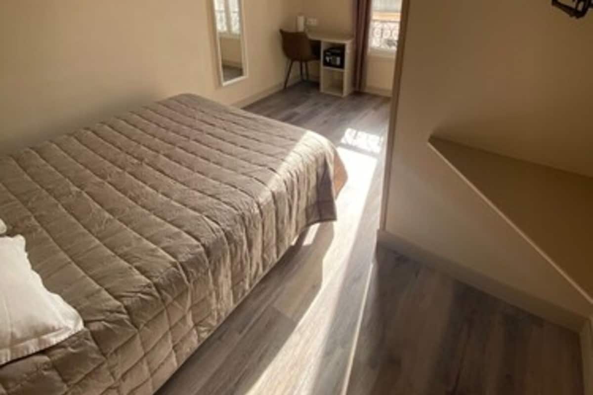 A bedroom with a bed, a desk, a chair, a TV, and a window with curtains.