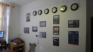 A room with multiple clocks displaying different time zones, a desk with a computer, and various framed pictures on the wall. - Lagan Backpackers (Belfast)