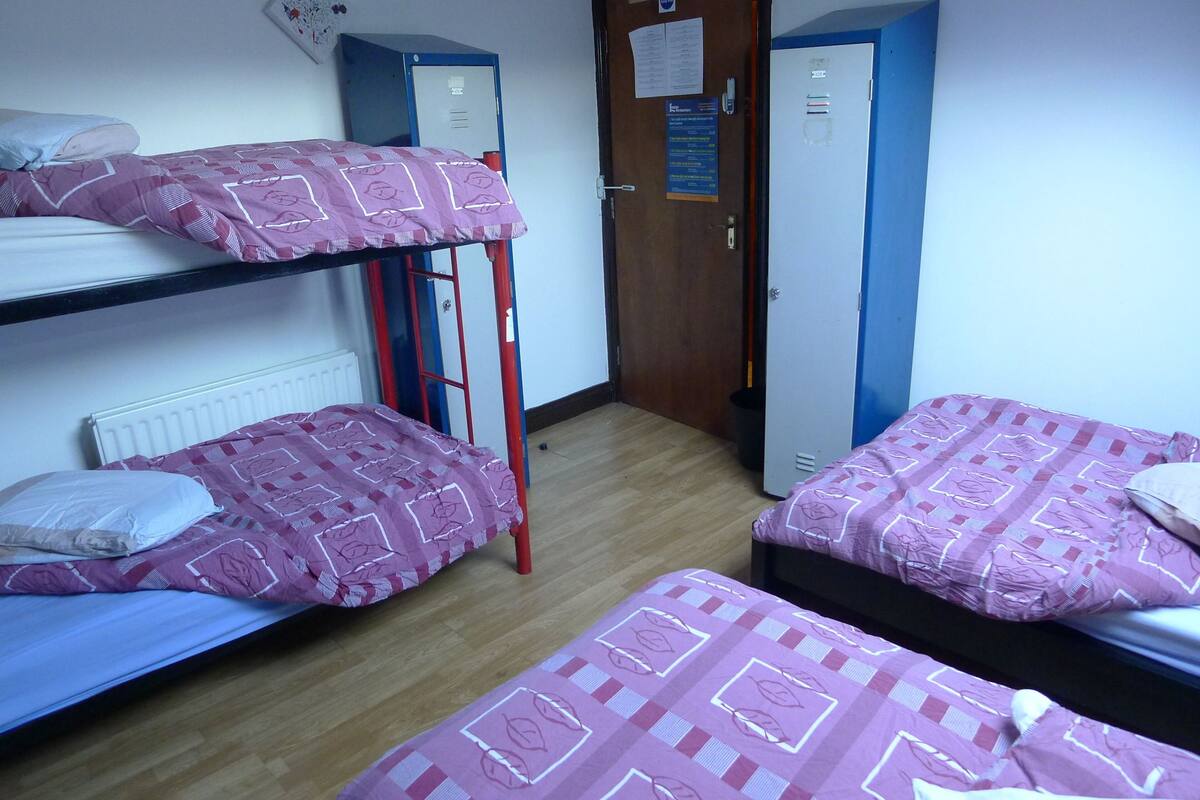 A dormitory room with bunk beds, a radiator, a wooden door, and a blue wardrobe.