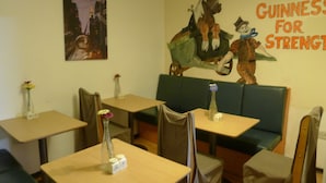 A restaurant interior with booths and tables, a mural on the wall, and a sign reading "GUINNESS FOR STRENGTH". - Lagan Backpackers (Belfast)