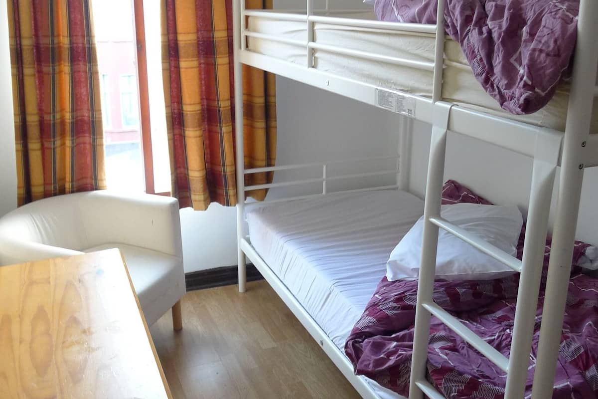 A bunk bed room with a wooden desk, plaid curtains, and a window.