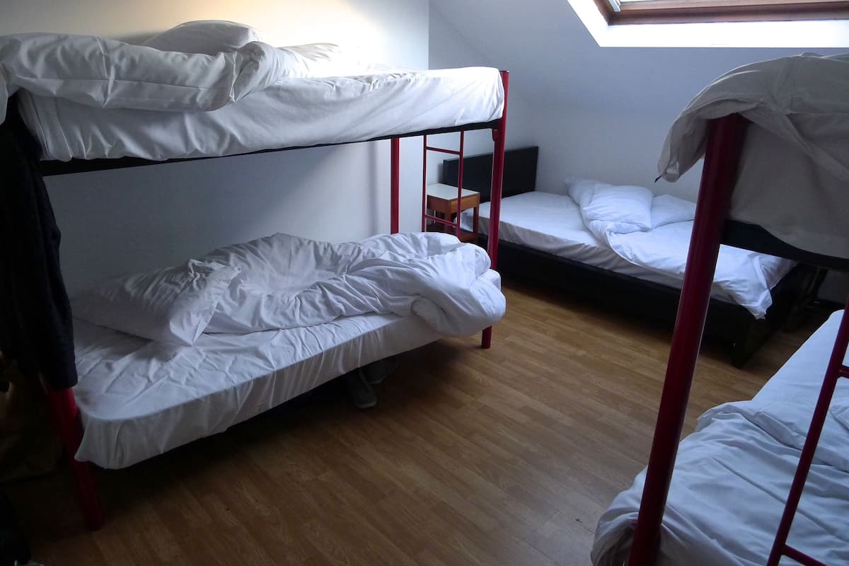 A dormitory room with bunk beds, a small wooden table, and a skylight.