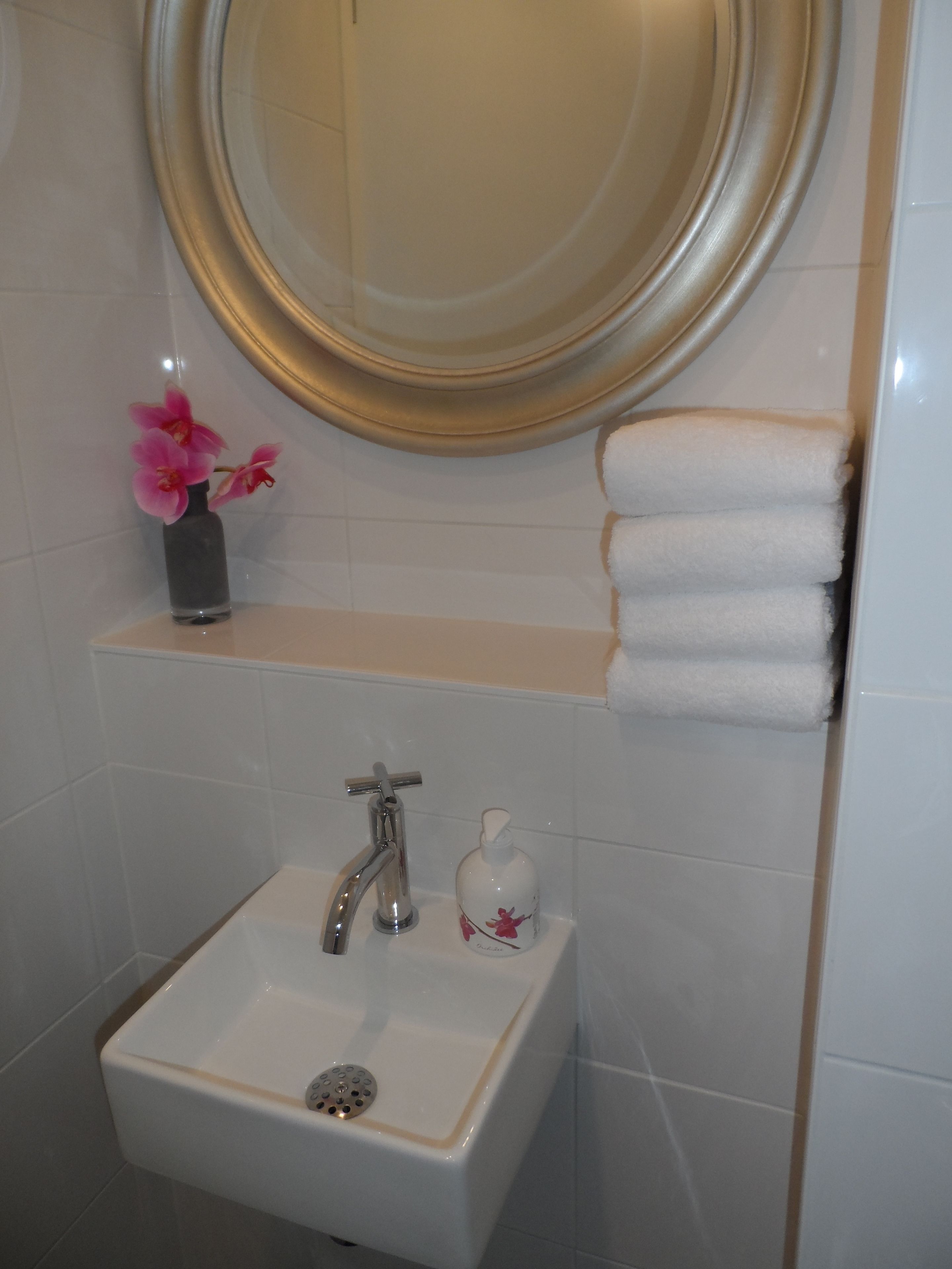 Une salle de bain avec un lavabo blanc, un miroir, un porte-serviettes et un vase contenant des fleurs roses.