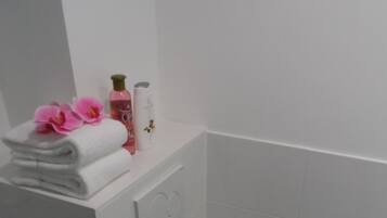 Une petite salle de bain avec des toilettes blanches, une pile de serviettes et quelques articles de toilette disposés sur une étagère.