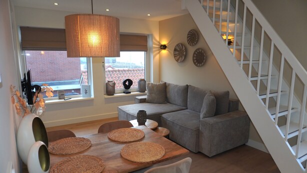Een moderne woonkamer met een houten eettafel, een grijze bank en een trap.