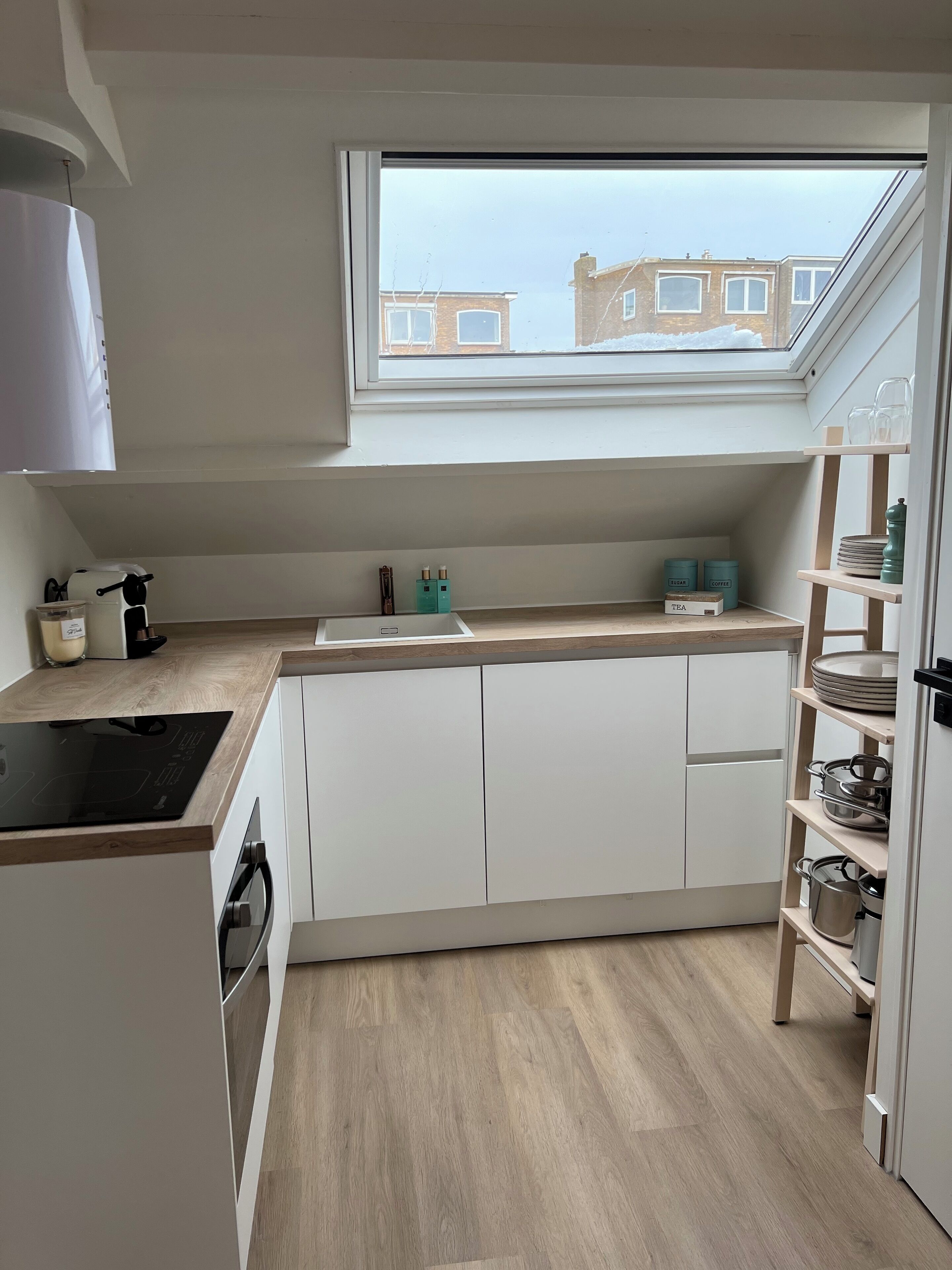 A modern kitchen with a skylight, white cabinets, a wooden countertop, and a view of buildings outside.