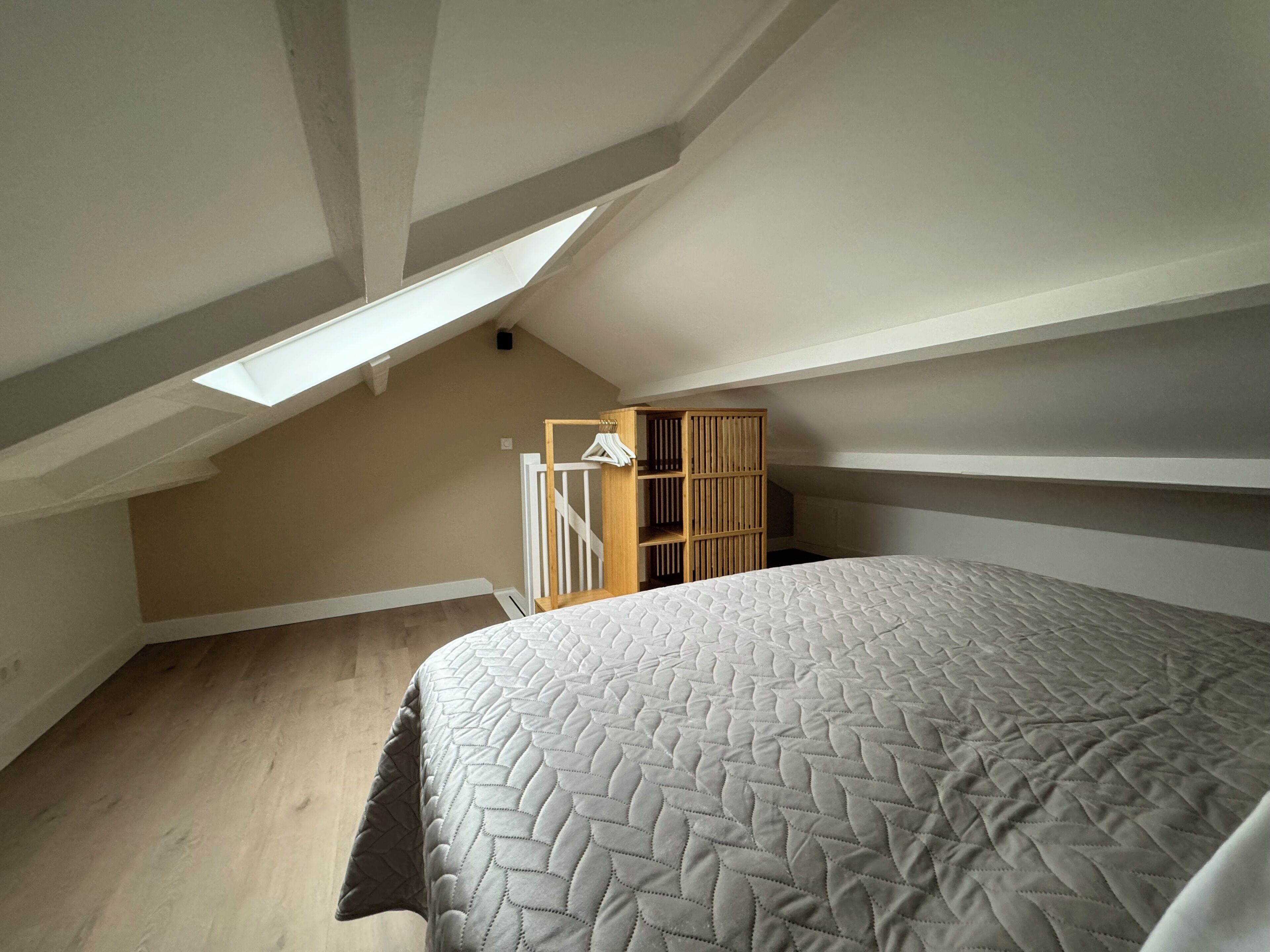 Un dormitorio con una cama grande, techo inclinado, armario de madera y tragaluz.