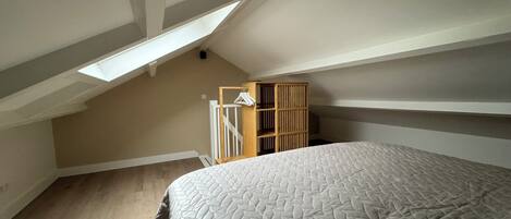 Un dormitorio con una cama grande, techo inclinado, armario de madera y tragaluz.