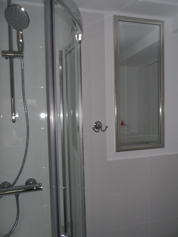 A glass-enclosed shower with a handheld showerhead and a wall-mounted faucet.