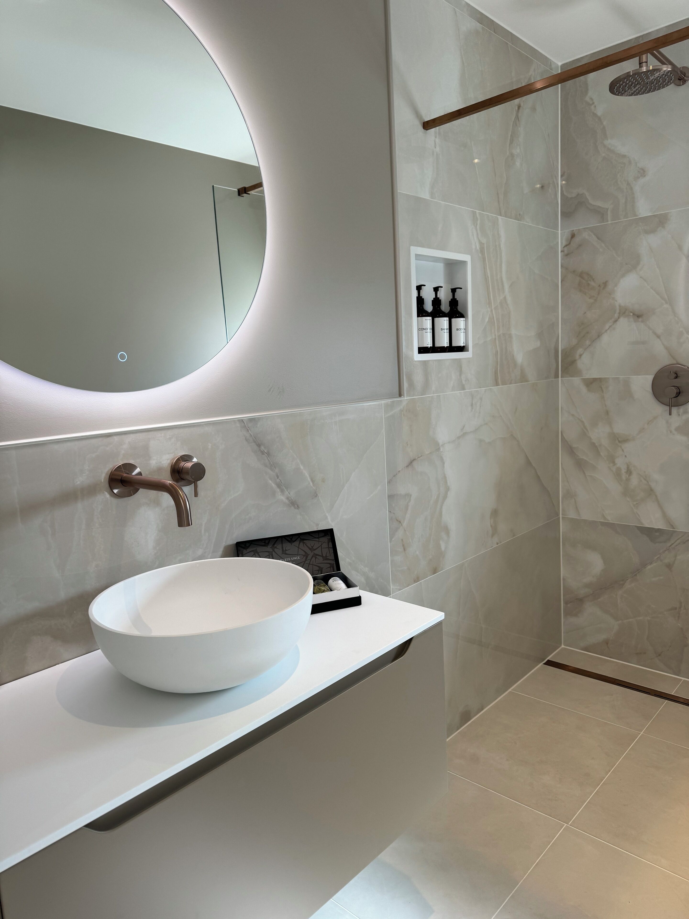 A modern bathroom with a large oval sink, a round mirror, and a shower area with a glass door.