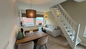 Een moderne woonkamer met een houten eettafel, twee stoelen, een bank en een trap met witte leuningen.