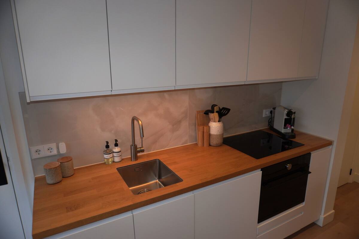 Een moderne keuken met witte kasten, een houten aanrecht, een roestvrijstalen spoelbak en een oven.