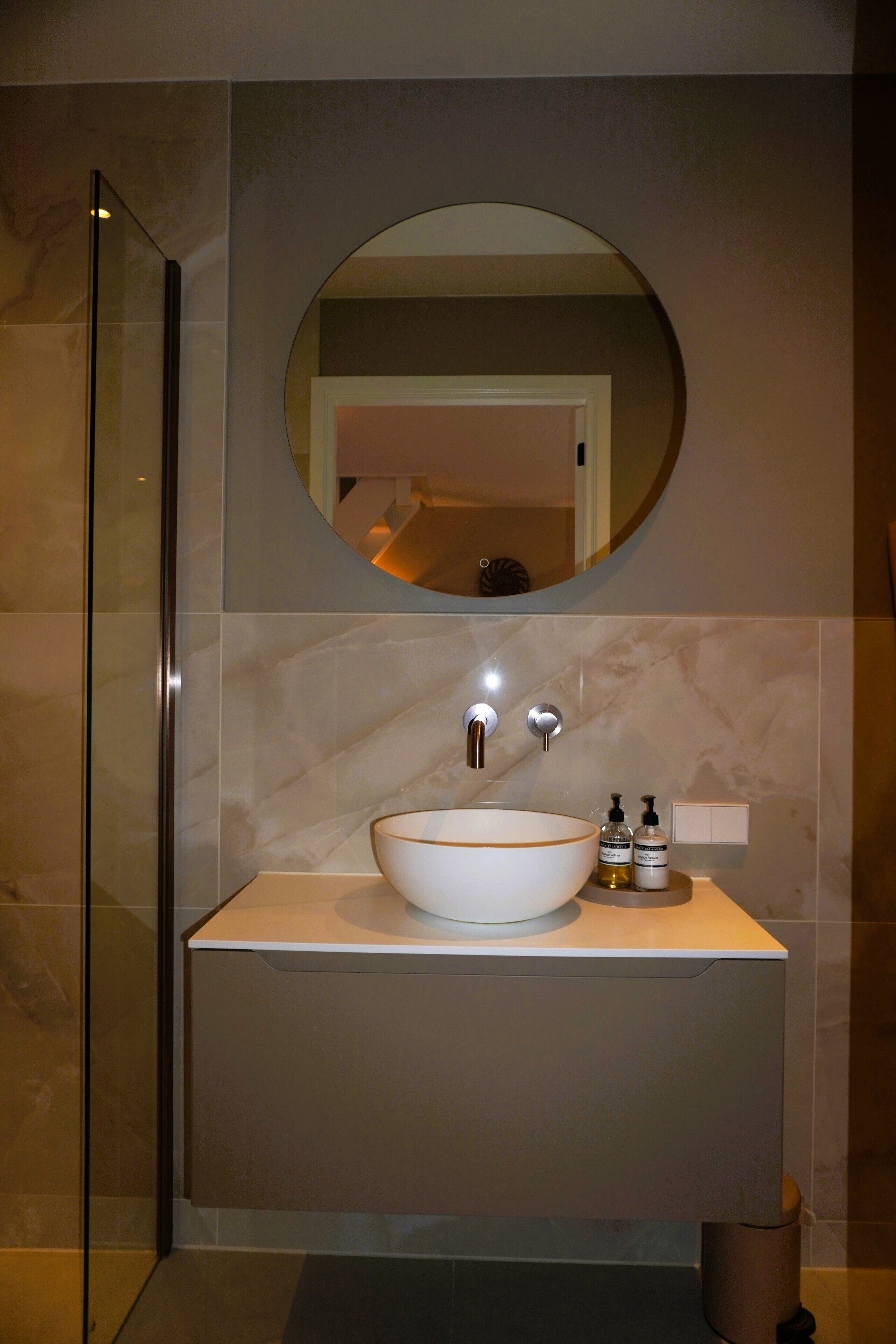 Une salle de bain moderne avec un grand miroir ovale, un lavabo sur colonne et une cabine de douche en verre.