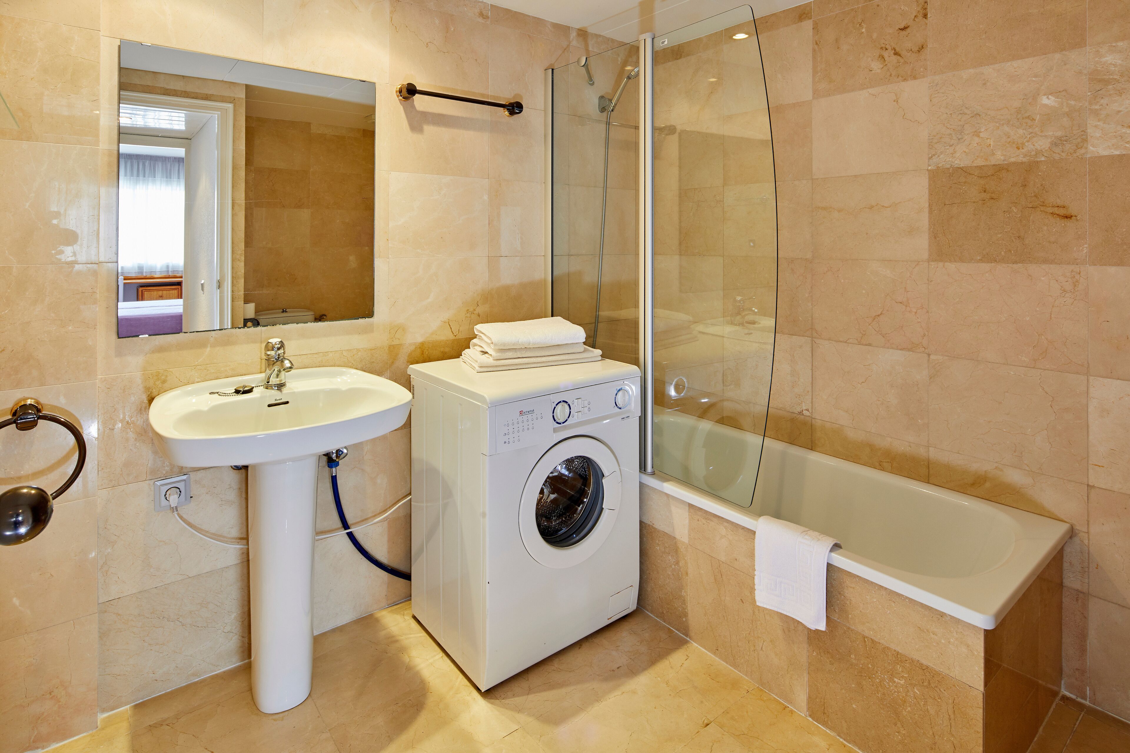 Un baño moderno con lavamanos, lavadora y cabina de ducha con paredes de vidrio.