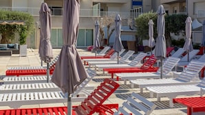 A poolside area with sun loungers and umbrellas, surrounded by a building with balconies. - Centremar (Torroella de Montgrí)