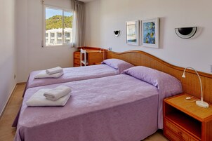 A hotel room with two beds, a desk, a chair, a lamp, and artwork on the walls.