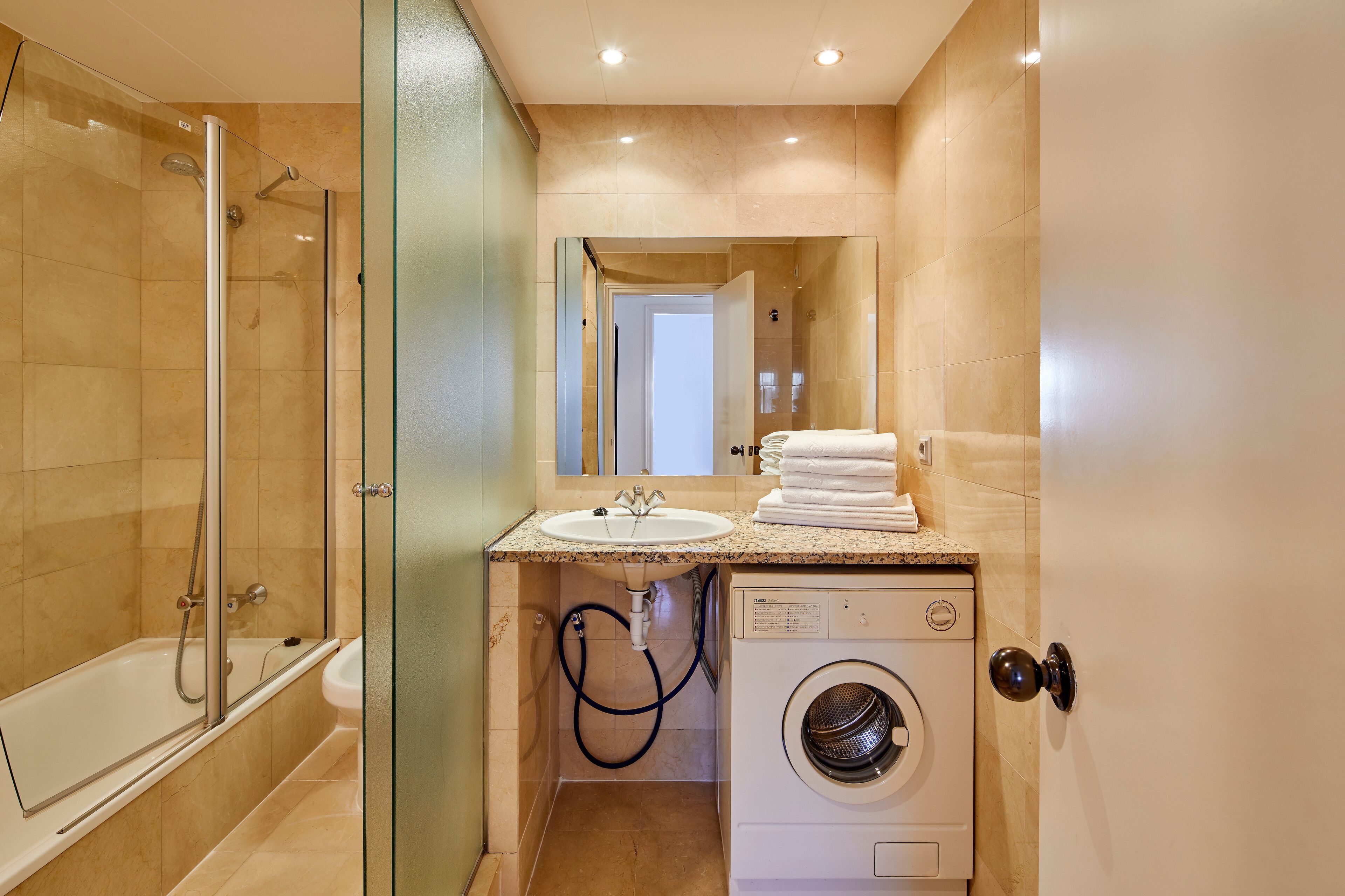 Un baño moderno con ducha acristalada, lavabo y lavadora integrada.