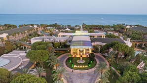 An aerial view of a resort with a central building, palm trees, and a view of the sea. - DOBEDAN WORLD PALACE - All inclusive (Kemer)