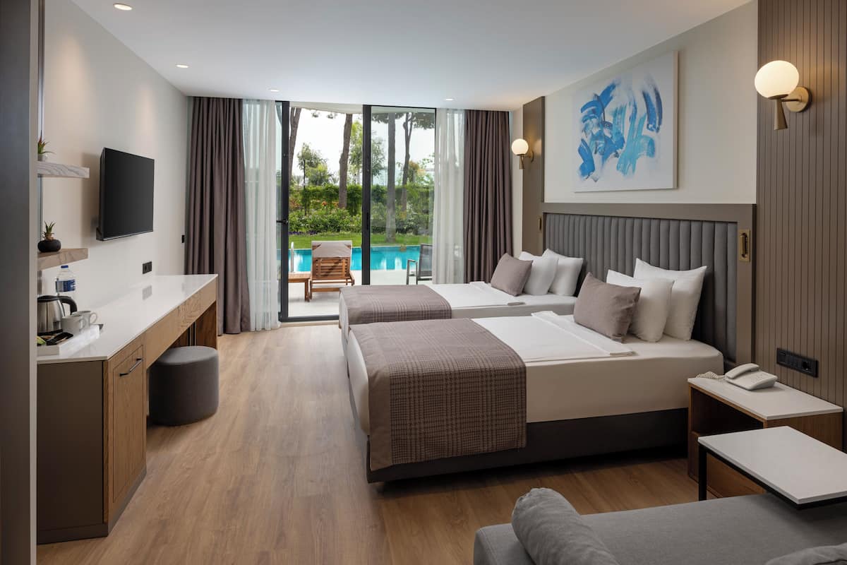 A modern hotel room with a large bed, a desk, a chair, and a view of a swimming pool.