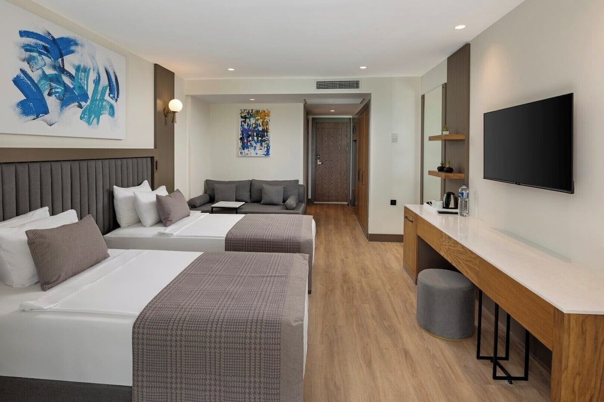 A hotel room with two beds, a desk, a TV, and artwork on the walls.